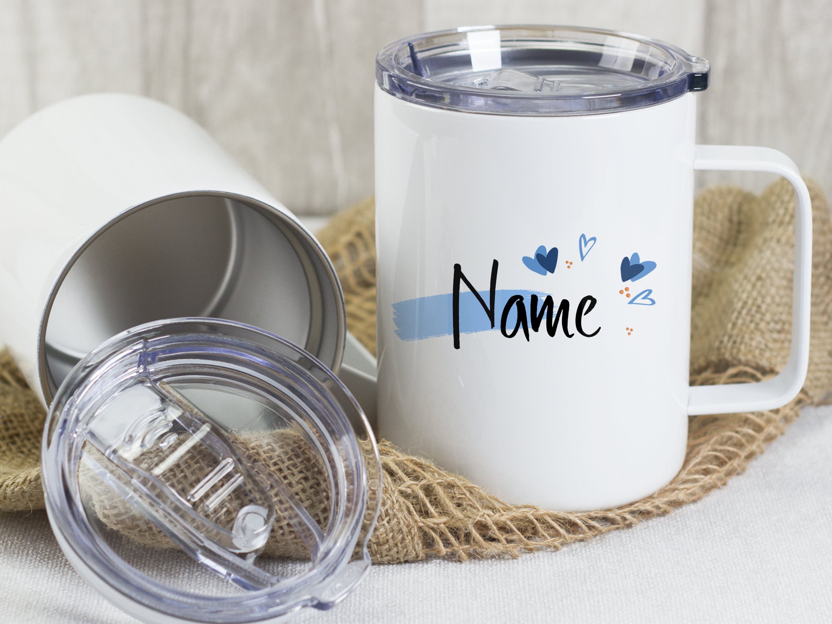 Weißer Becher mit personalisierbarem Namen und blauen Herzen.