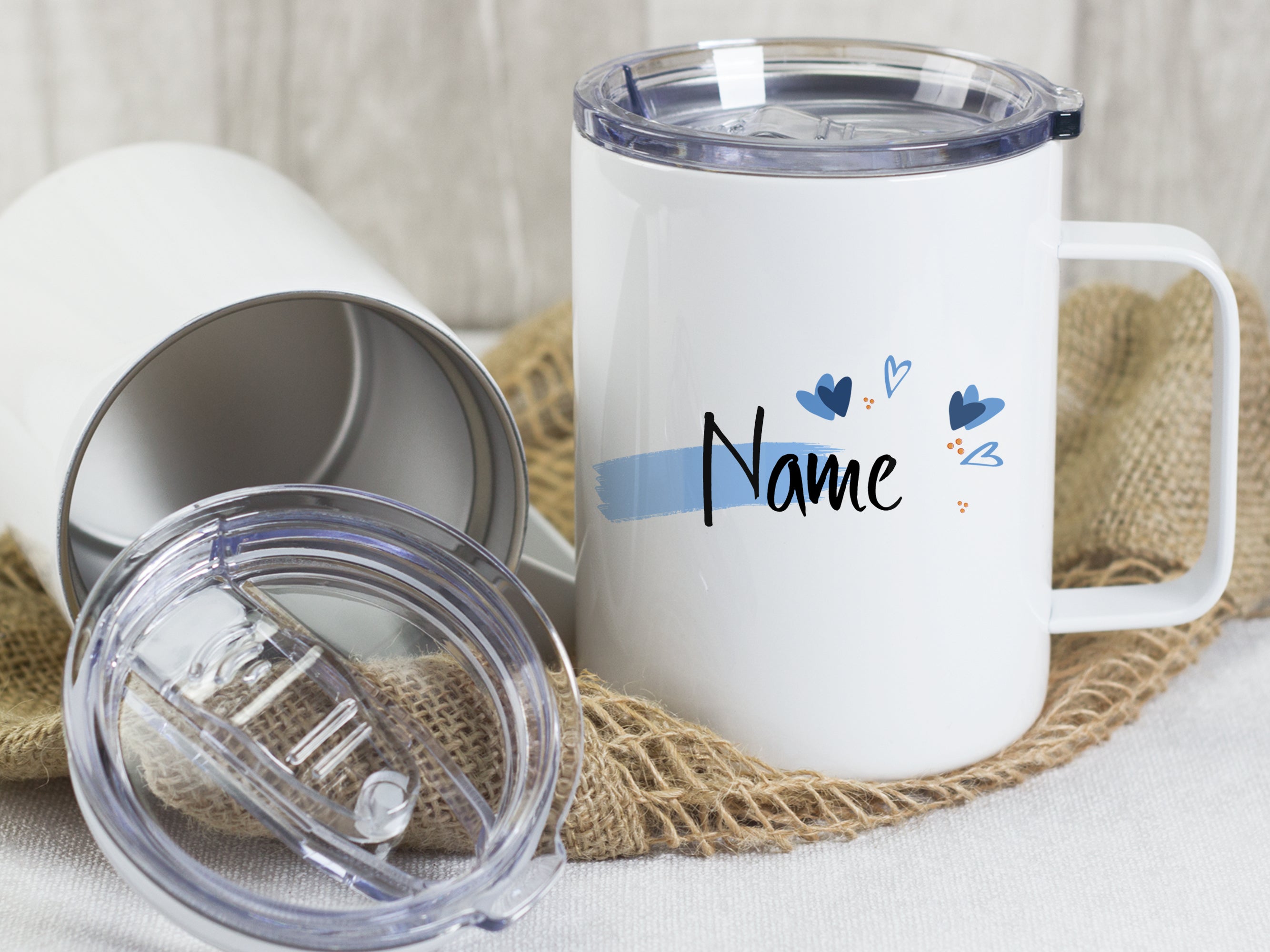 Weißer Becher mit personalisierbarem Namen und blauen Herzen.