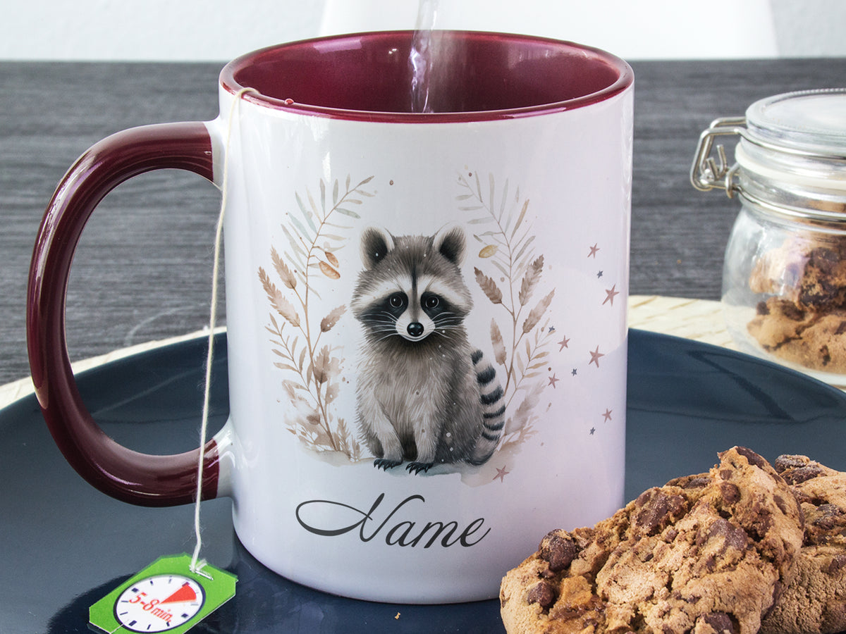 Kaffeetasse mit Waschbär-Motiv und bordeauxrotem Henkel.