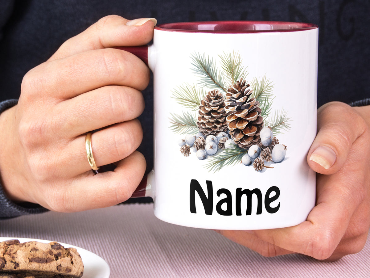 Weißer Becher mit Tannenzapfen und personalisiertem Namen.