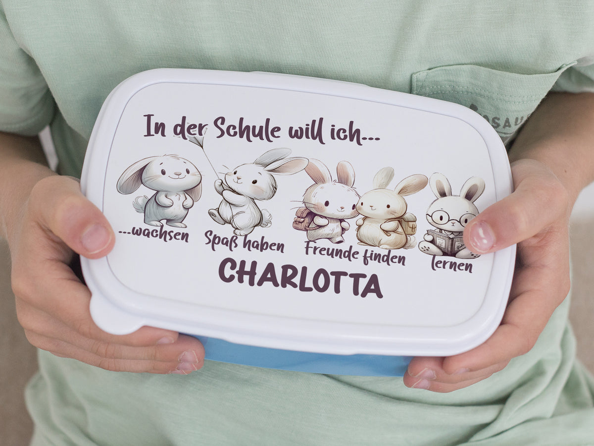 Bento-Box in Weiß mit bunten Hasen und Text.