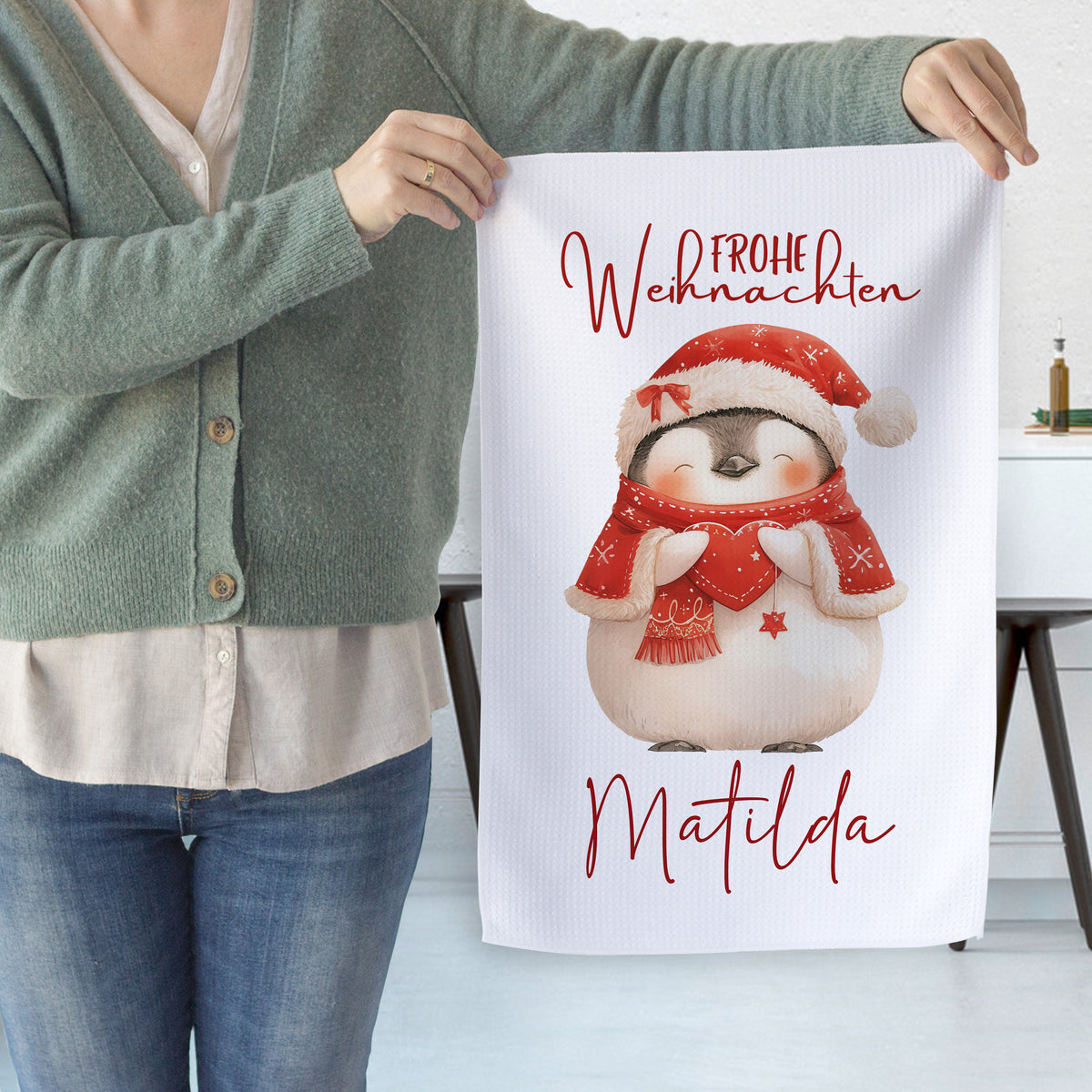 Weihnachtliches Geschirrtuch mit Pinguin und rotem Schriftzug.