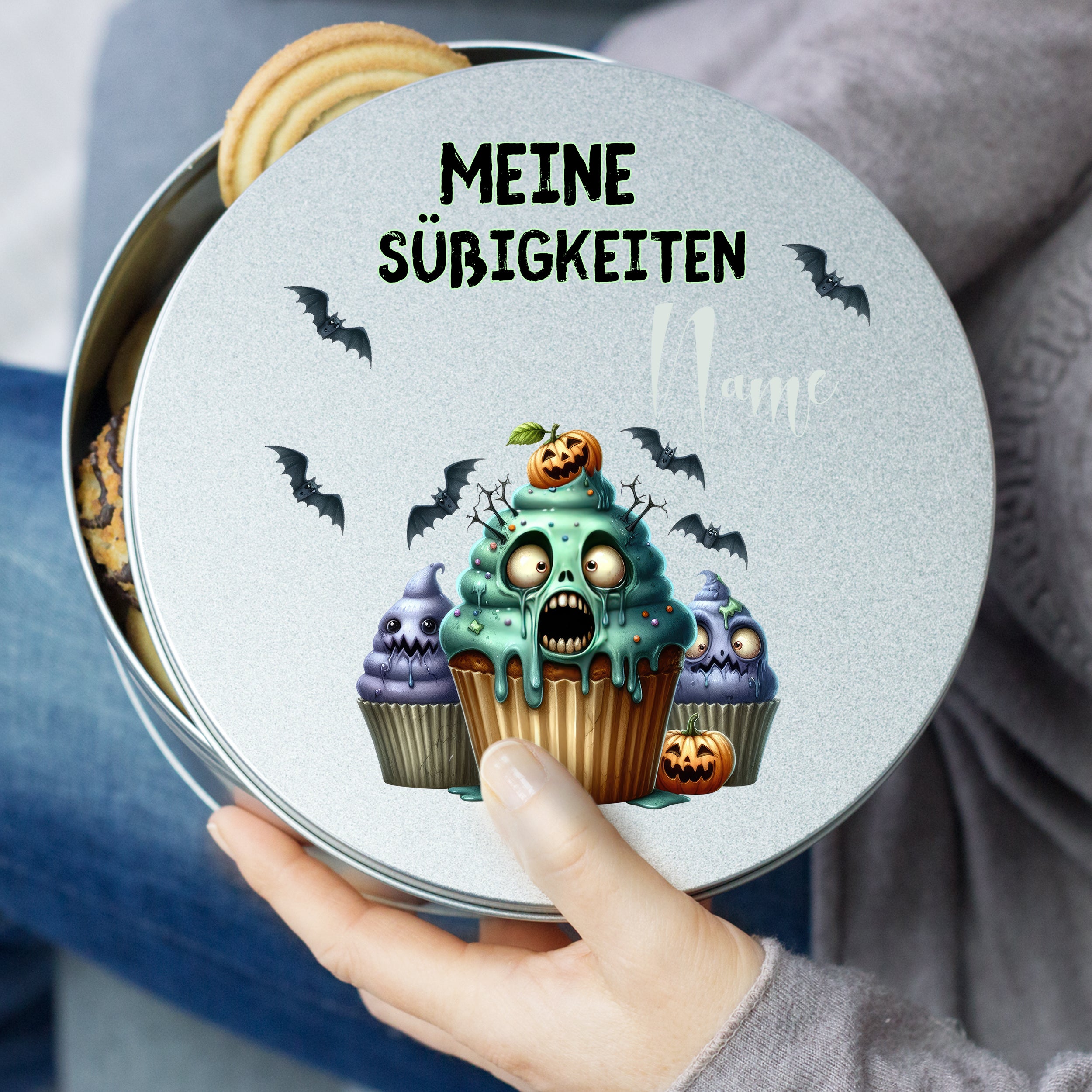 Graue Keksdose mit gruseligen Cupcakes und Schriftzug.