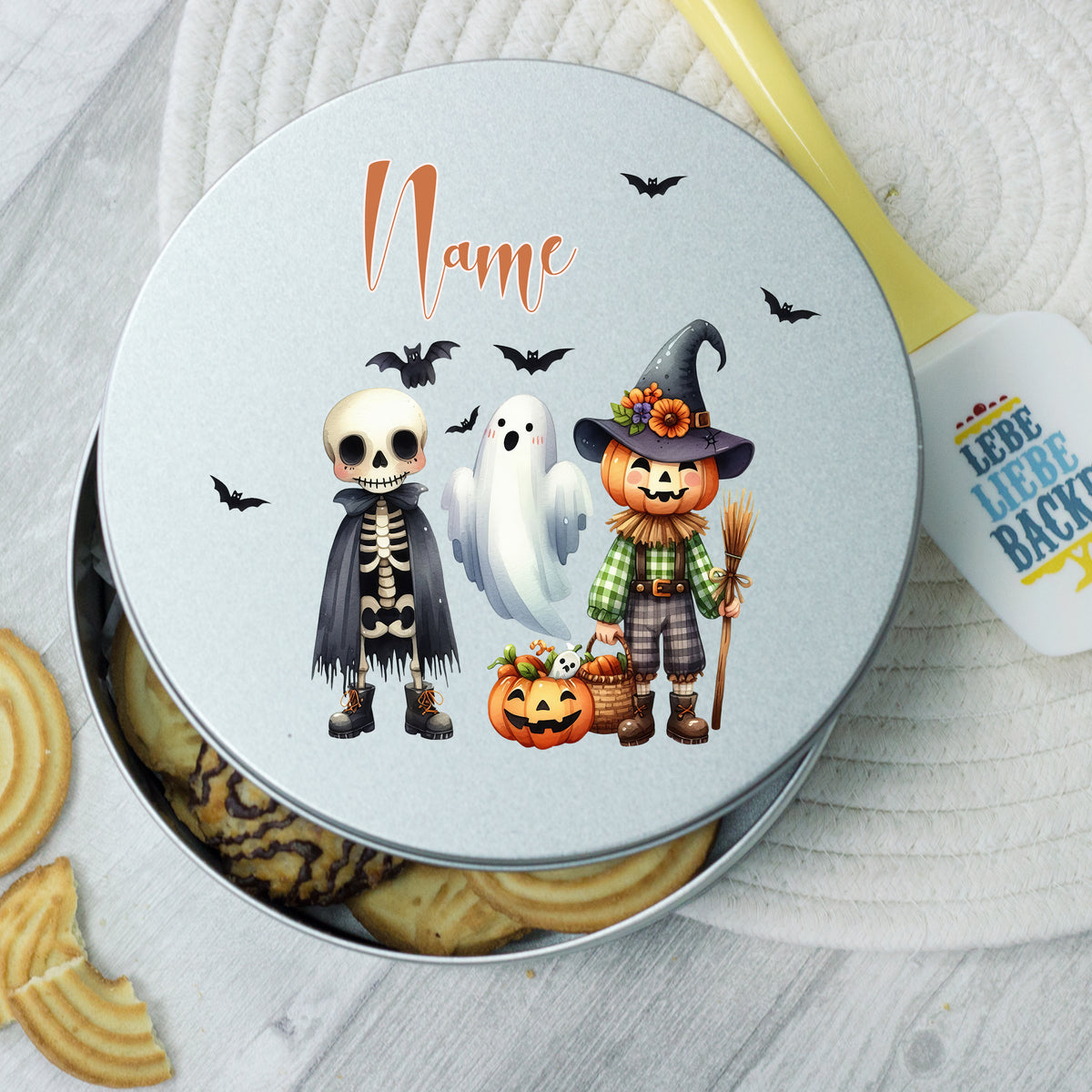 Runde Keksdose mit Halloween-Motiven: Skelett, Geist, Kürbis.
