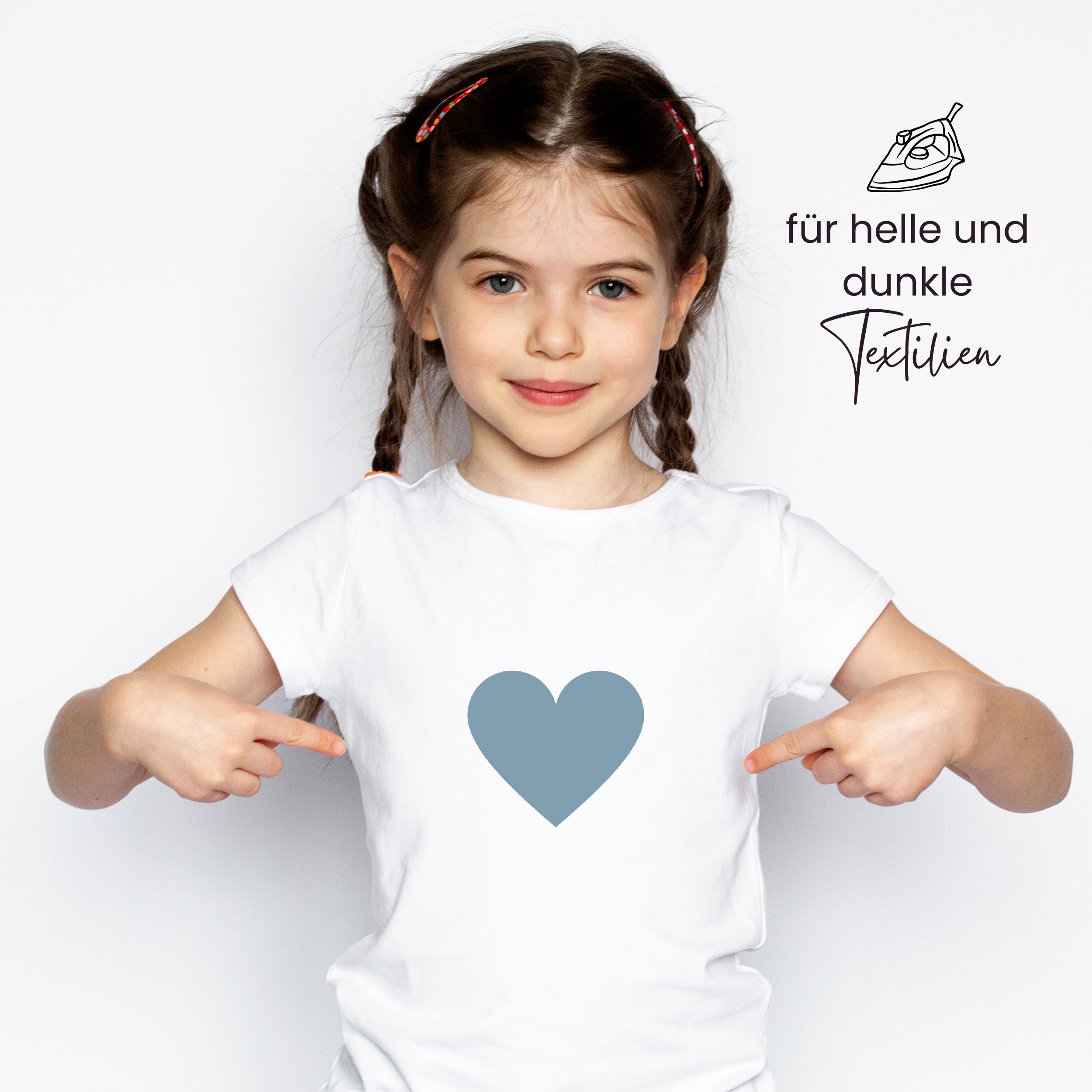 Weißes T-Shirt mit blauem Herzmotiv, Mädchen zeigt darauf.