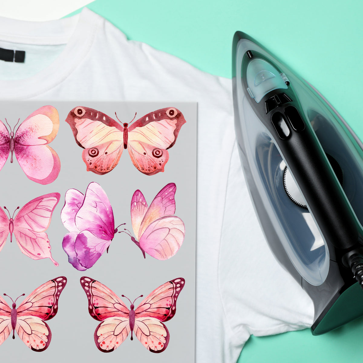Weißes T-Shirt mit rosa Schmetterlingsmotiven und Dampfbügeleisen.