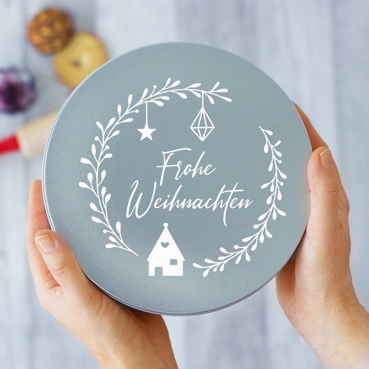 Graue Weihnachtsdose mit weißem Schriftzug und Dekoration.