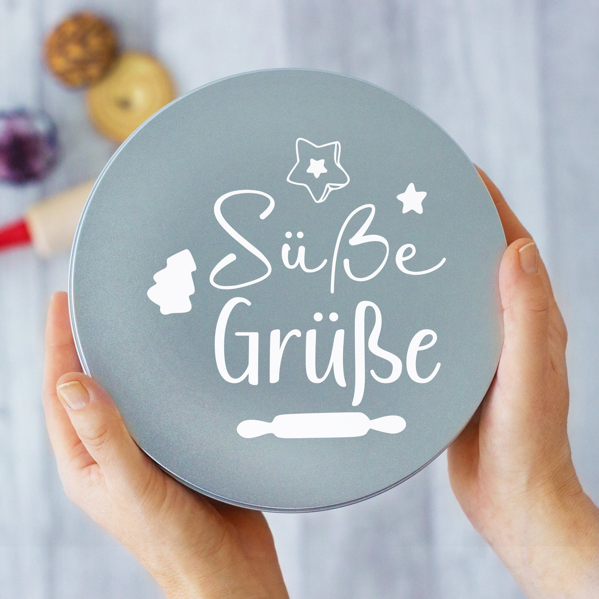 Graue Dose mit Aufschrift "Süße Grüße" und Backutensilien.