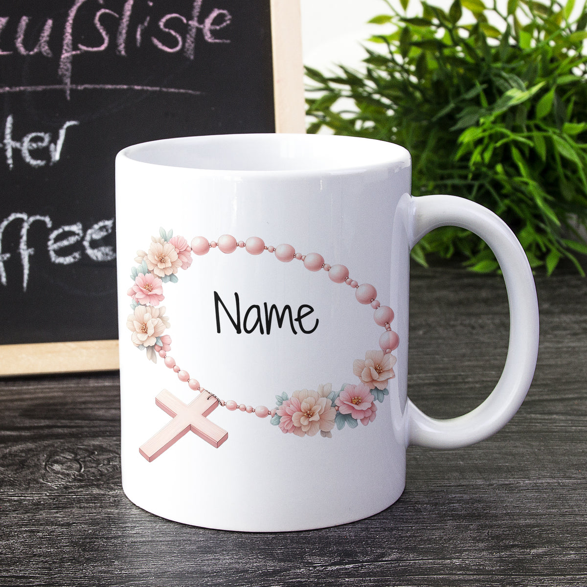 Weißer Kaffeebecher mit rosafarbenem Blumenkranz und Kreuz.