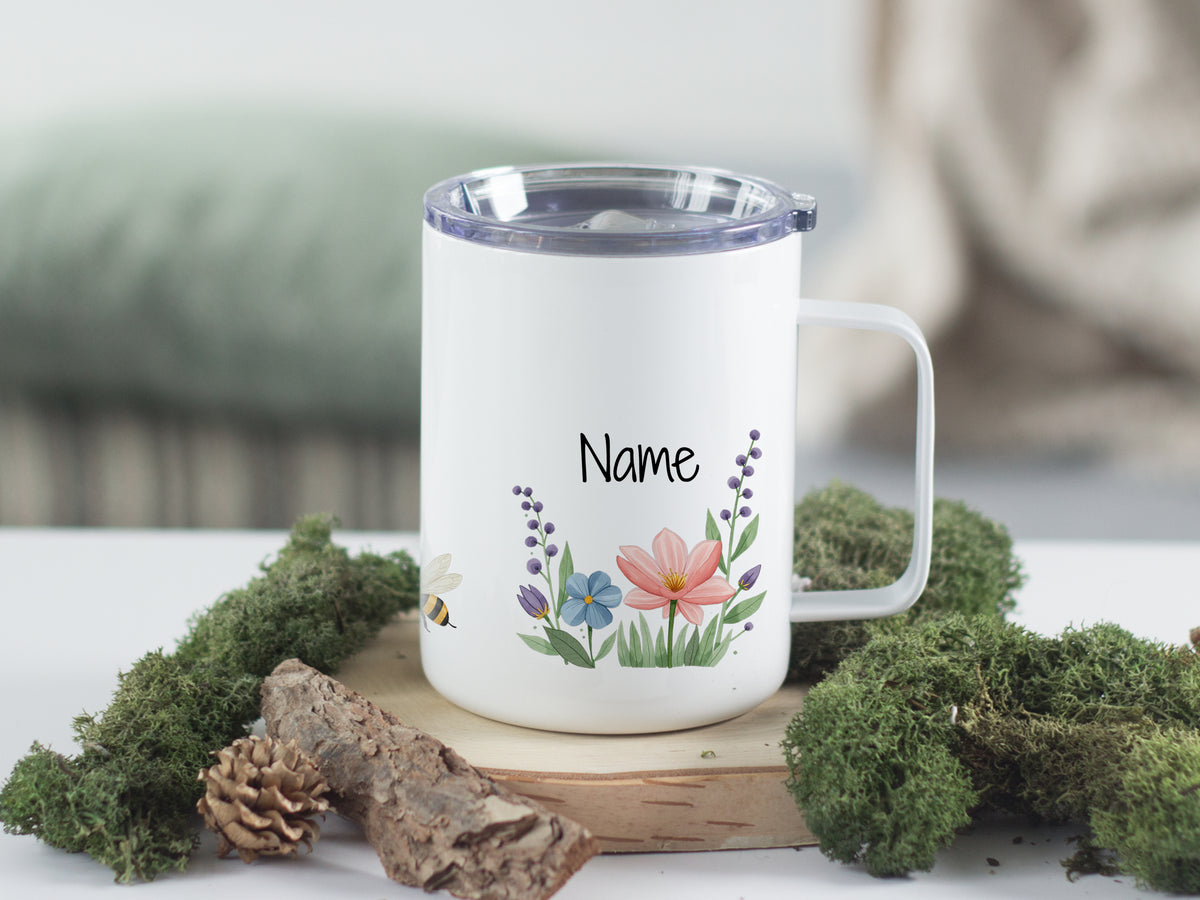 Weißer Becher mit bunten Blumen und personalisiertem Namen.