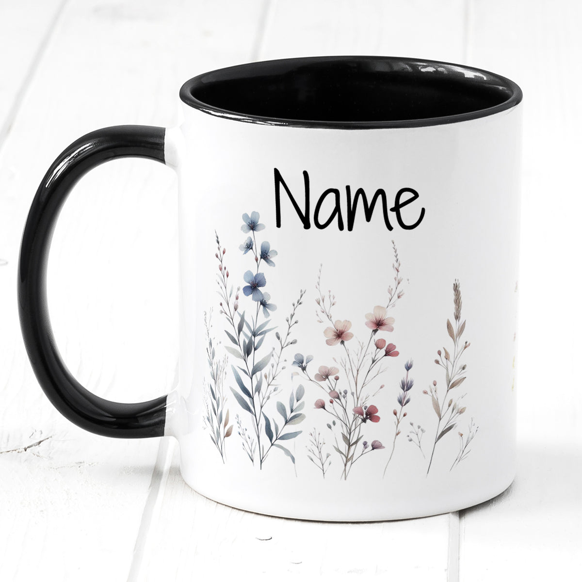 Tasse mit schwarzem Henkel, floralen Motiven und personalisierbarem Namen.