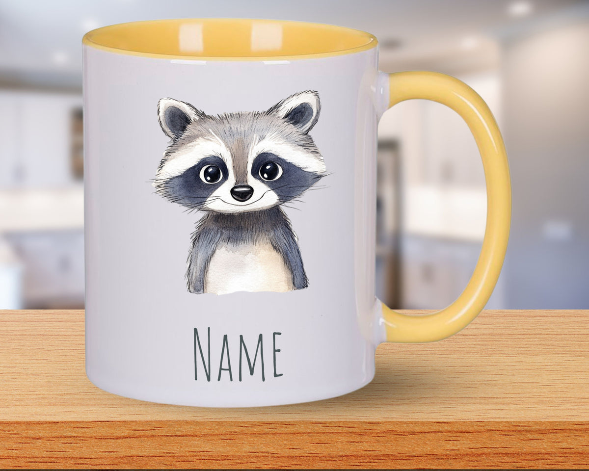 Tasse mit Waschbär-Motiv und gelbem Henkel.