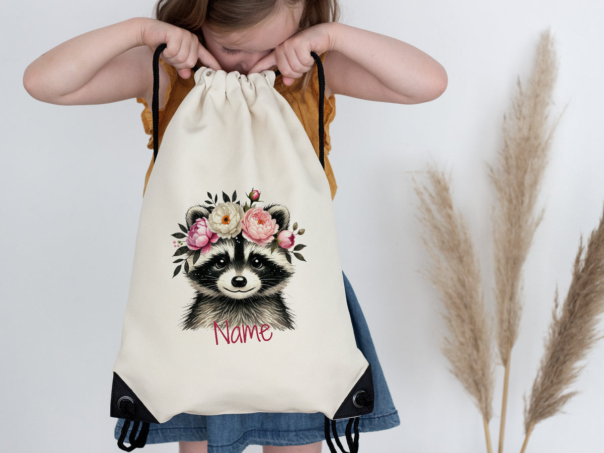 Beige Turnbeutel mit Waschbär und Blumenkranz.