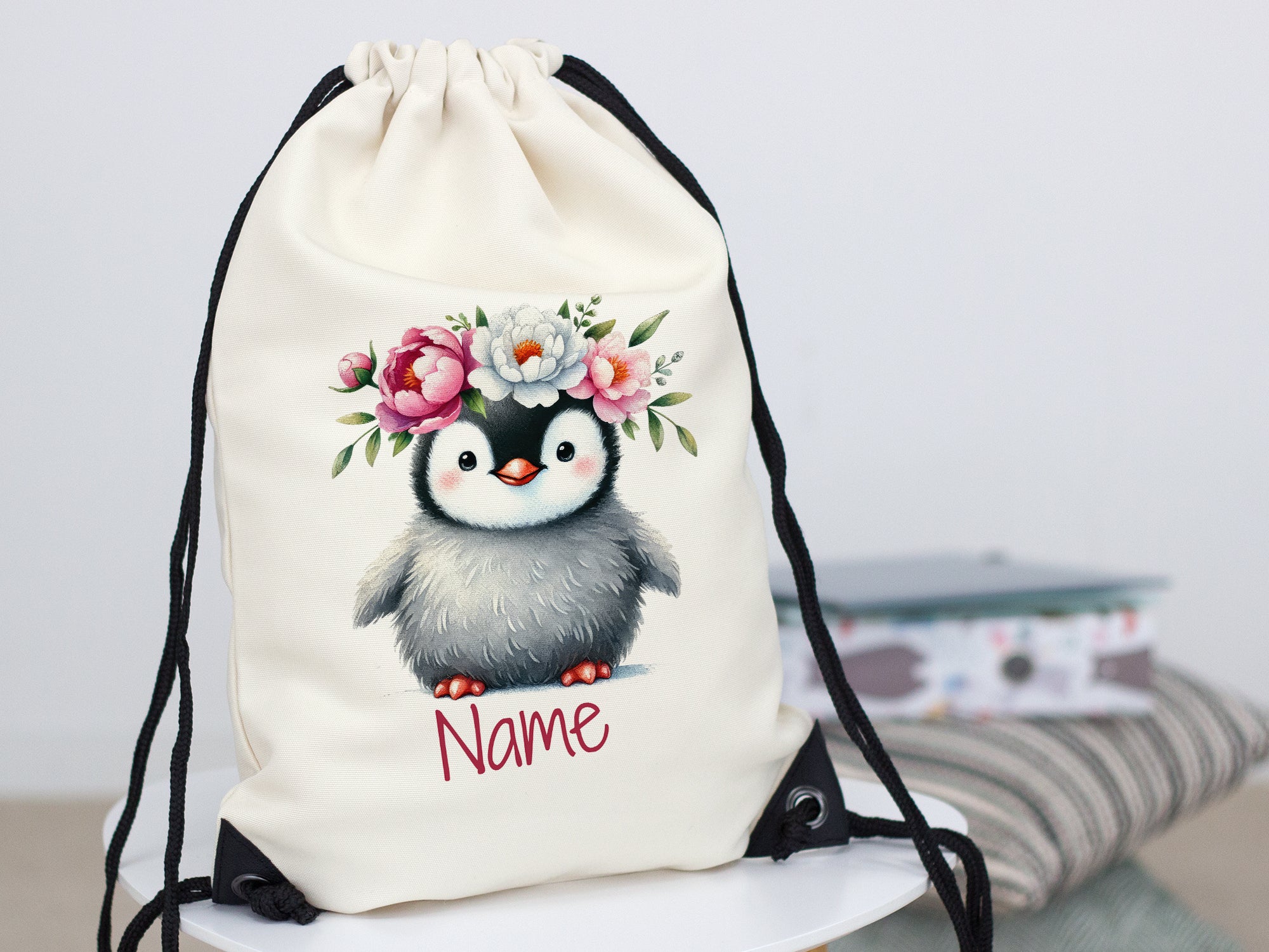 Beige Turnbeutel mit Pinguin und Blumenmotiv.