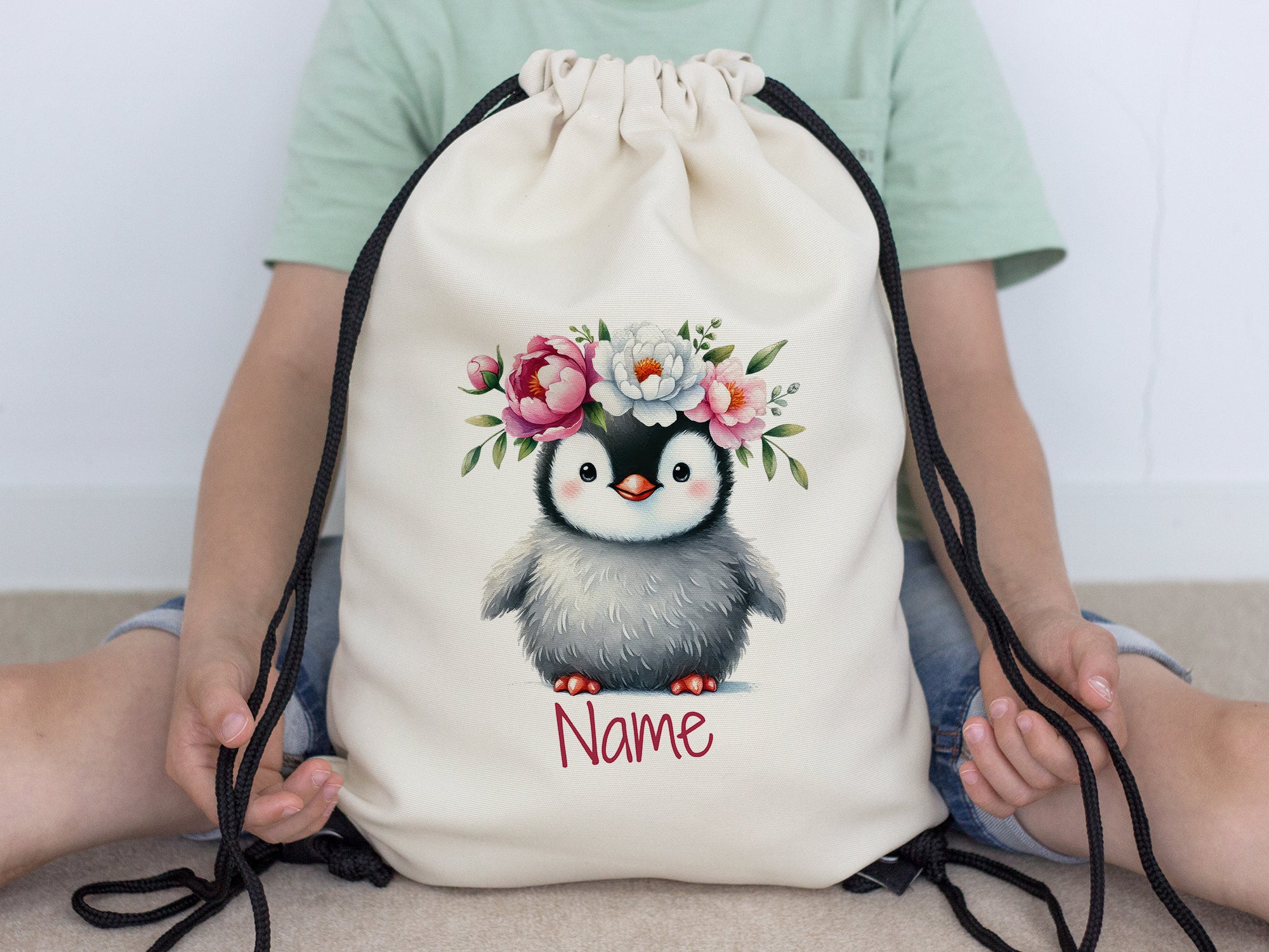 Beige Turnbeutel mit Pinguin und Blumenmotiv.