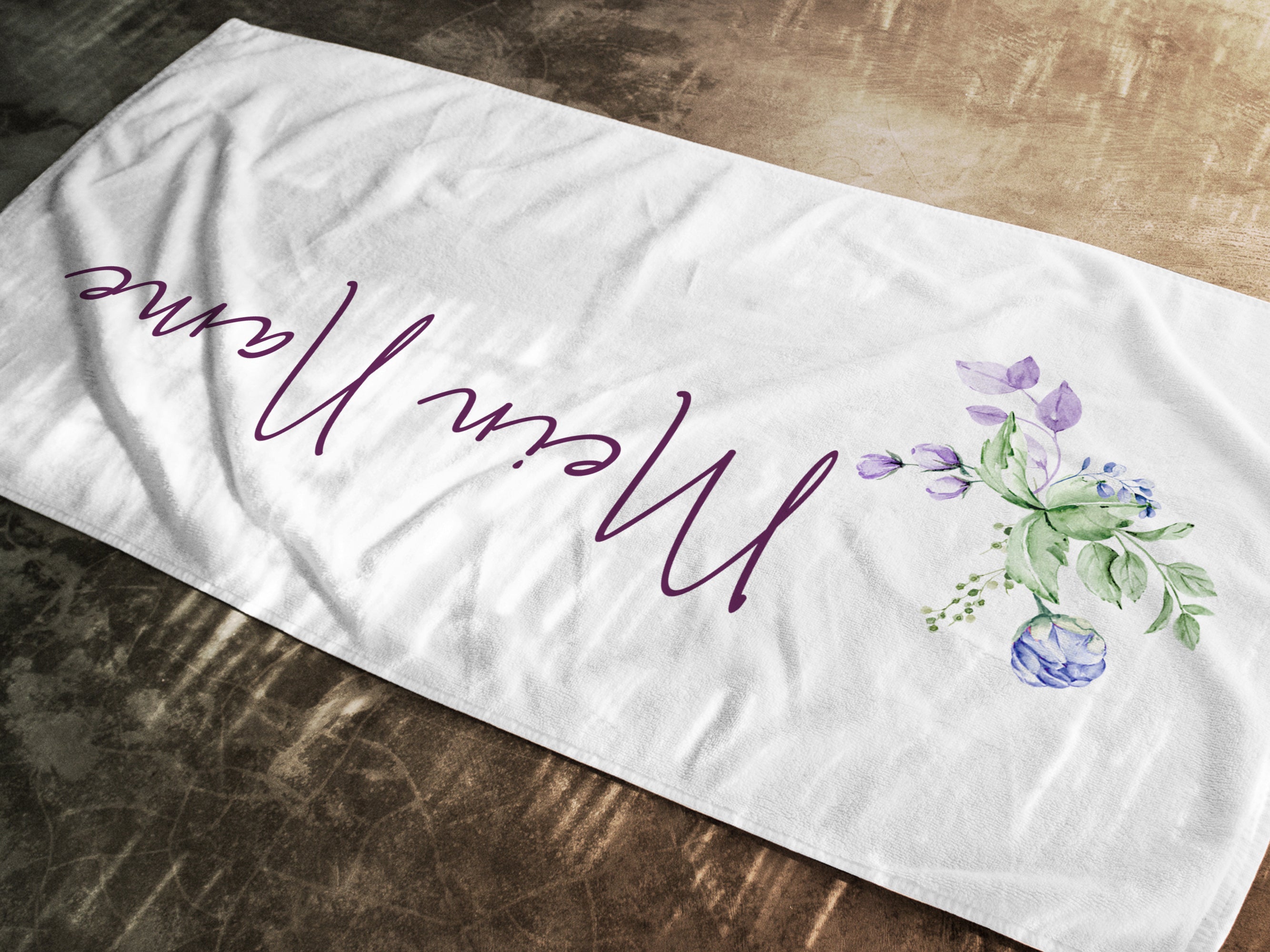 Weißes Handtuch mit floralem Design und Schriftzug.