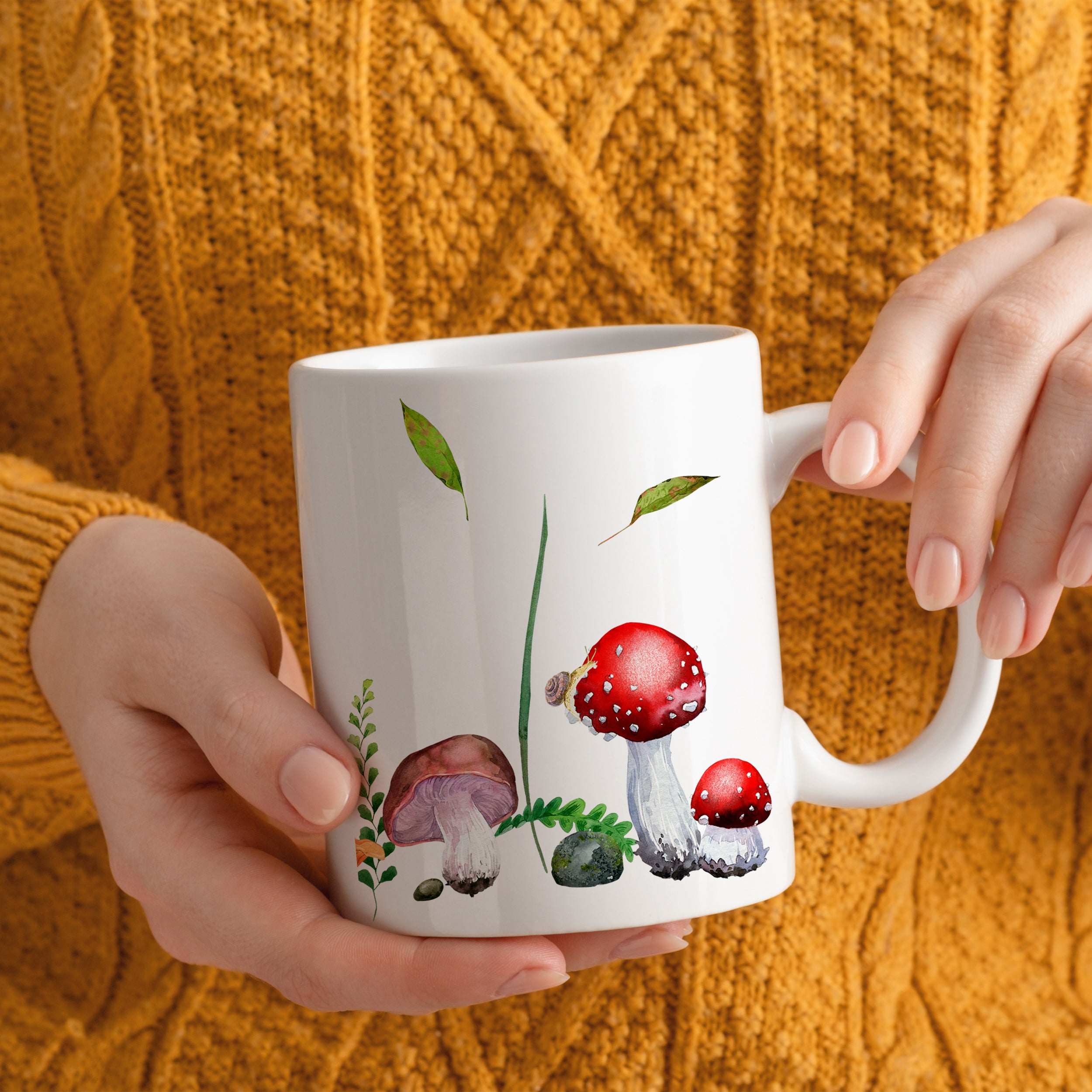 Weiße Tasse mit roten Fliegenpilzen und grünen Blättern.