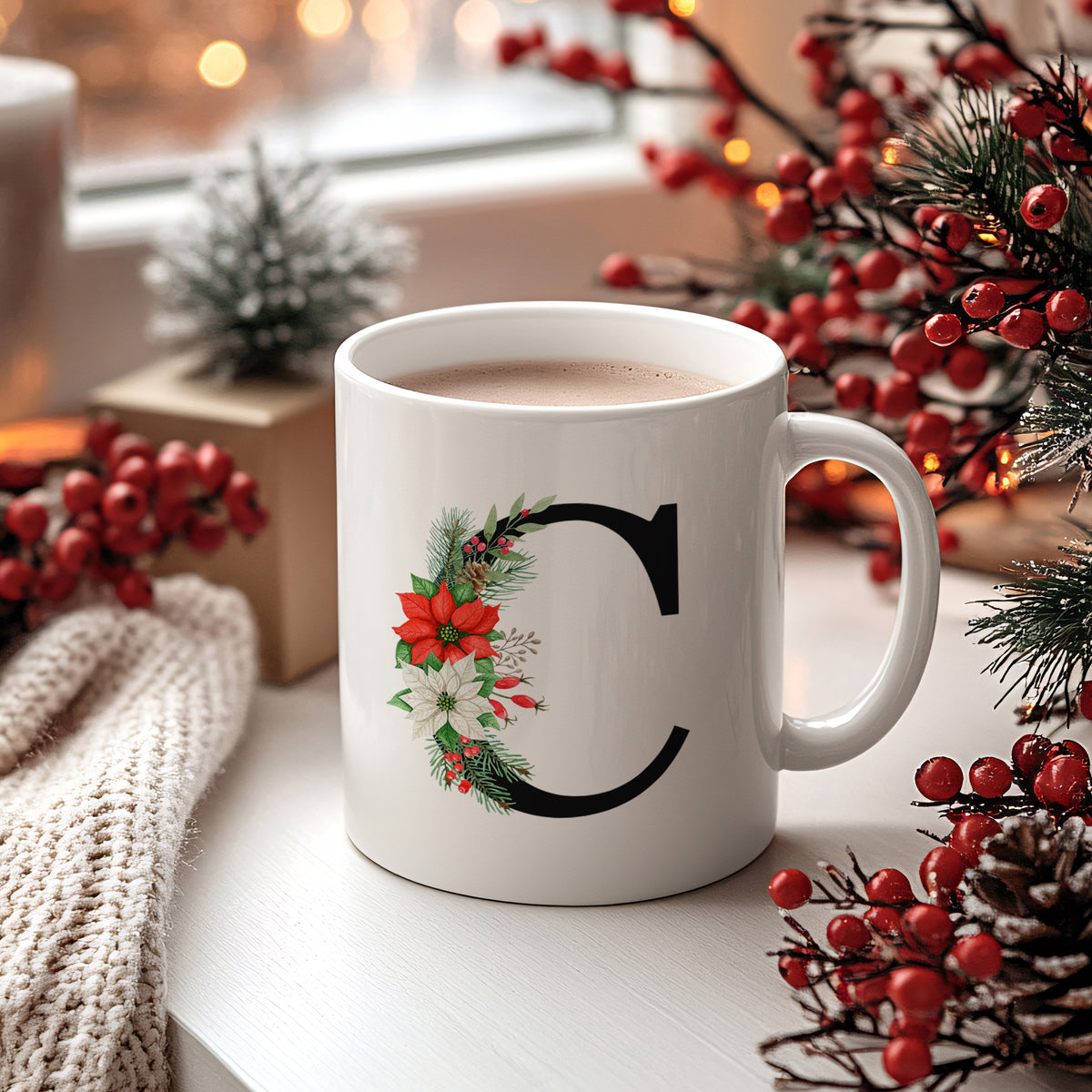 Weißer Becher mit schwarzem Buchstaben "C" und Weihnachtsdeko.