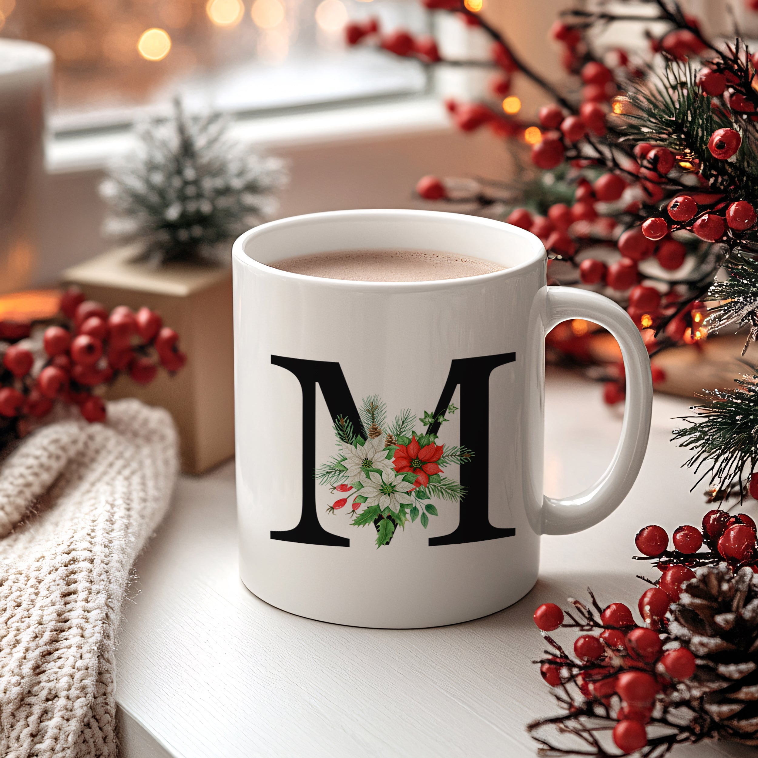 Weiße Tasse mit floralem M und Weihnachtsdesign.