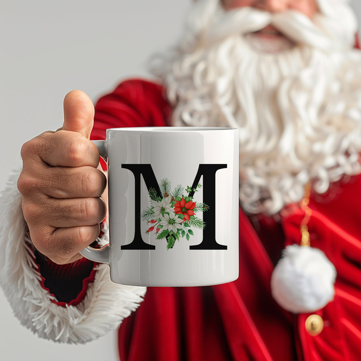 Weißer Becher mit schwarzem "M" und Weihnachtsmotiven.