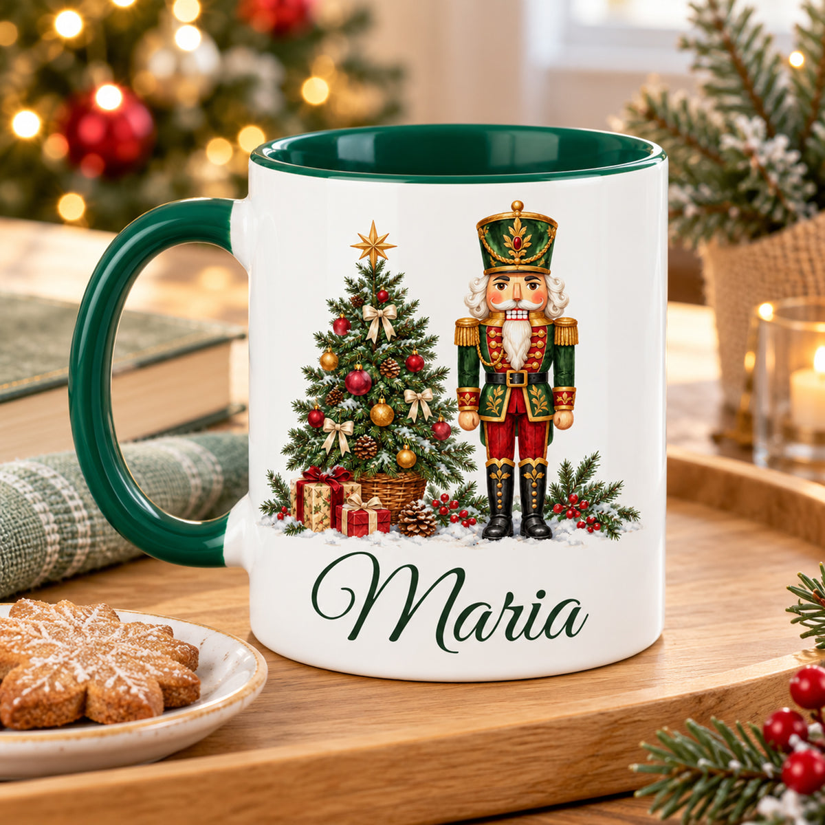 Weiße Keramiktasse mit grünem Henkel und grüner Innenseite, Motiv Tannenbaumwächter und Wunschname auf einem Tablett mit Gebäck in weihnachtlicher Umgebung.