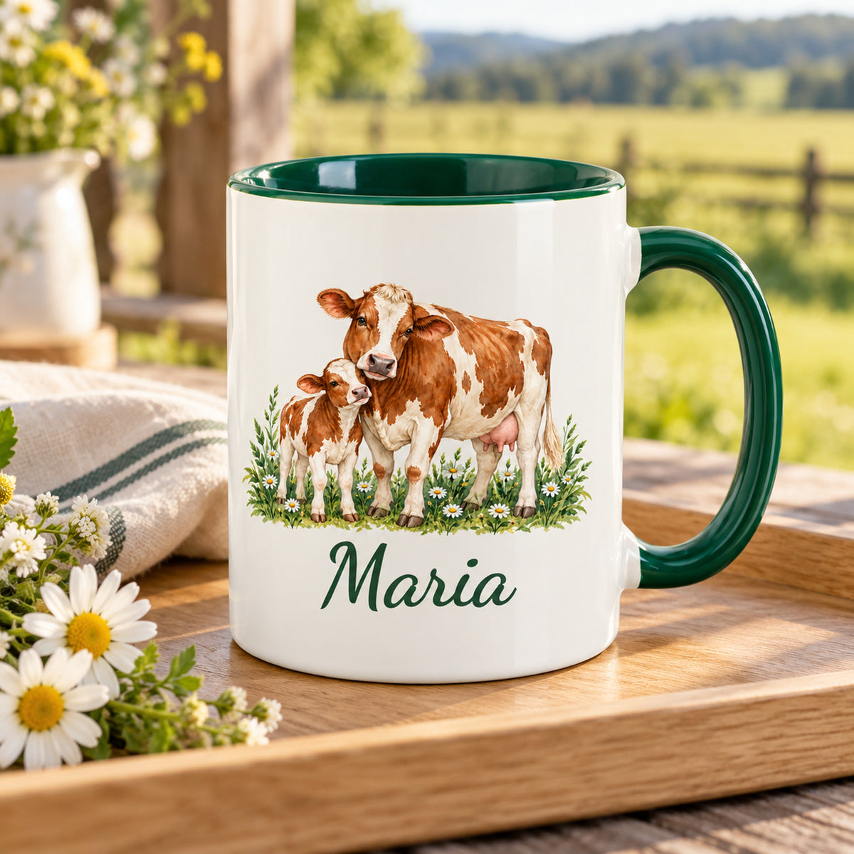 Kuh-Tasse mit braun-weißer Kuh und Kälbchen zwischen Wiesenblumen und Wunschname auf einem Holztablett mit Stoffserviette und Wiesenblumen