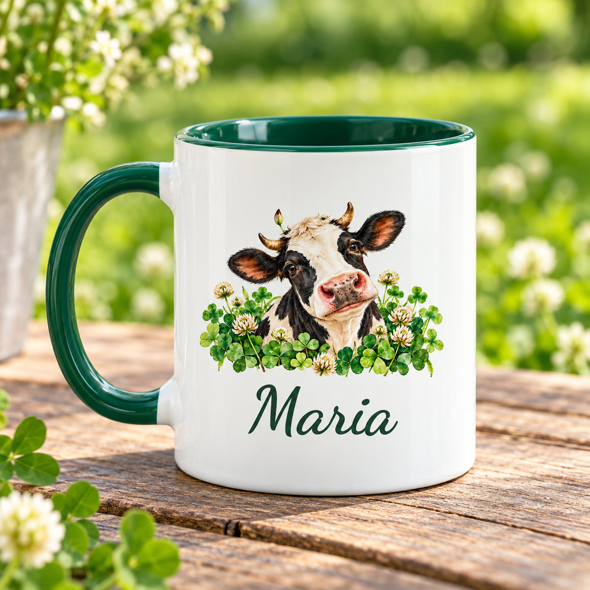 Kuh-Tasse mit schwarz-weißer Kuh zwischen Kleeblättern und Blüten und Wunschname mit Henkel links, gegenüberliegende Druckseite im Grünen