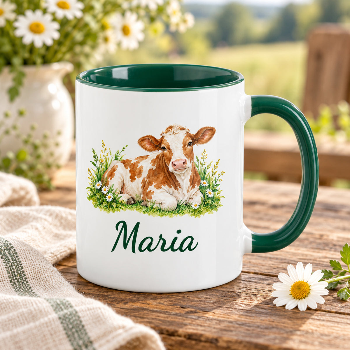 Kuh-Tasse mit ruhender braun-weißer Kuh mit Gänseblümchen und Wunschname auf einem Holztisch mit Wiesenblumen