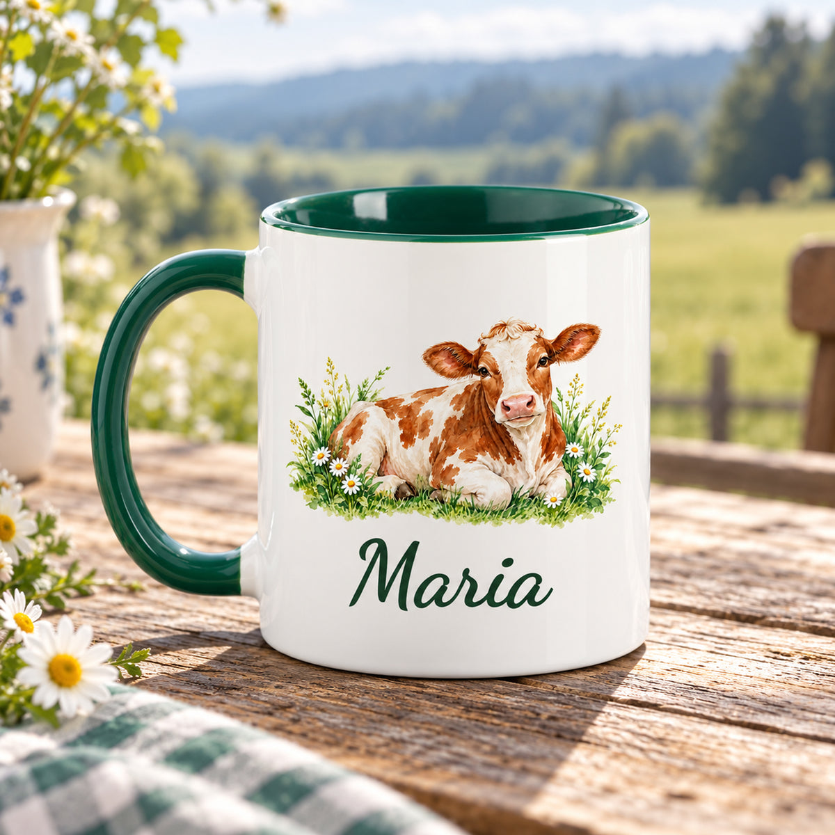 Kuh-Tasse mit ruhender braun-weißer Kuh mit Gänseblümchen und Wunschname mit Henkel links, gegenüberliegende Druckseite im Grünen
