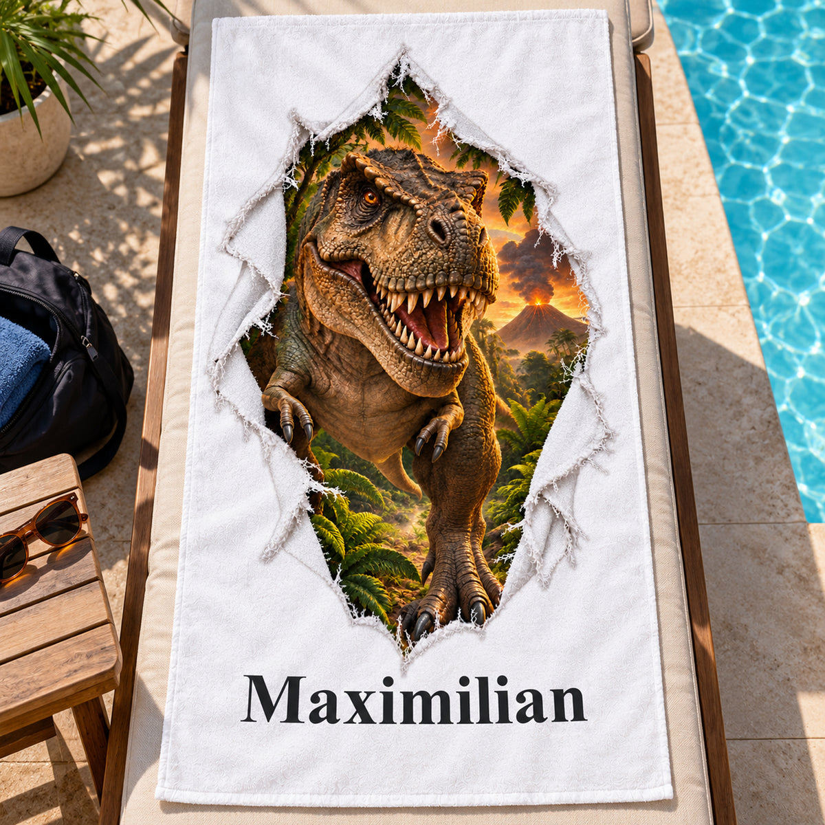 Weißes personalisiertes Handtuch mit T-Rex-Motiv im Stoffriss-Design auf einer Poolliege neben dunkler Sporttasche und Sonnenbrille.