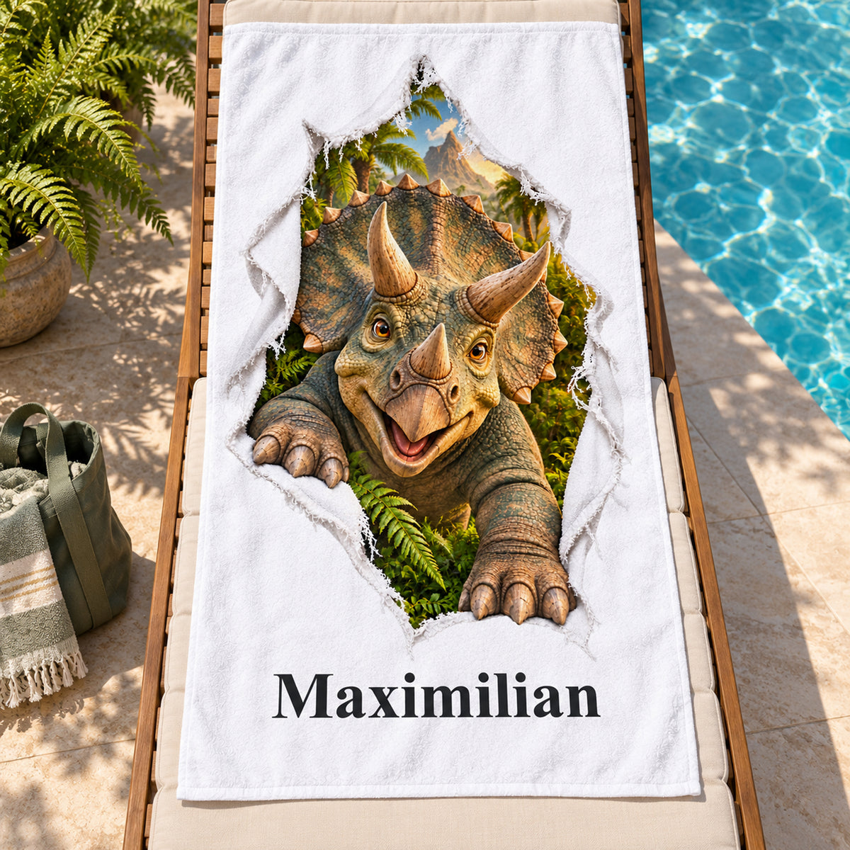 Weißes personalisiertes Handtuch mit Triceratops-Motiv im Stoffriss-Design auf einer Holzliege am Pool mit Farnen und grüner Tasche.