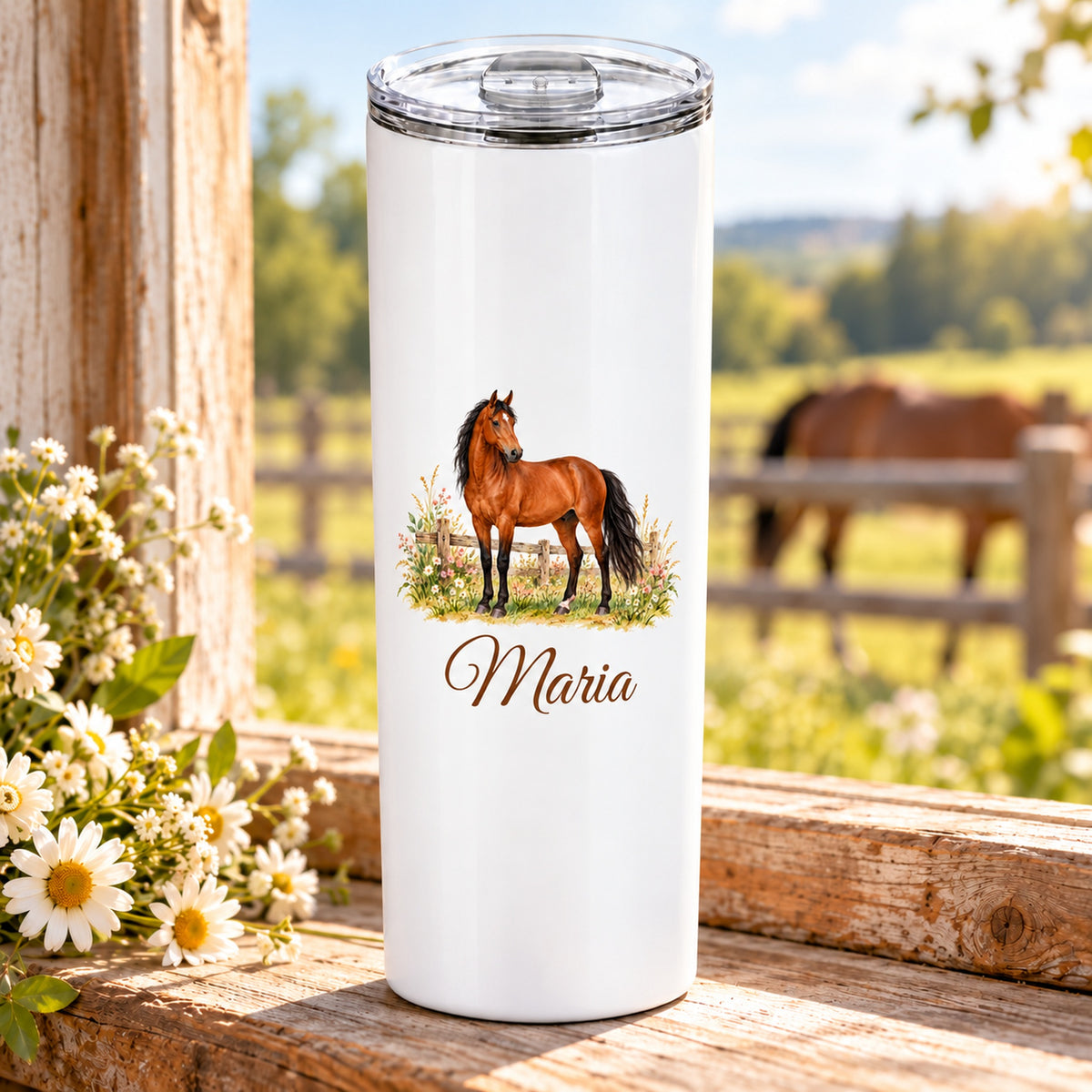 Weißer Thermobecher mit einem braunen Pferd am Koppelzaun und Wunschname auf einem Holztisch vor einer Pferdekoppel.